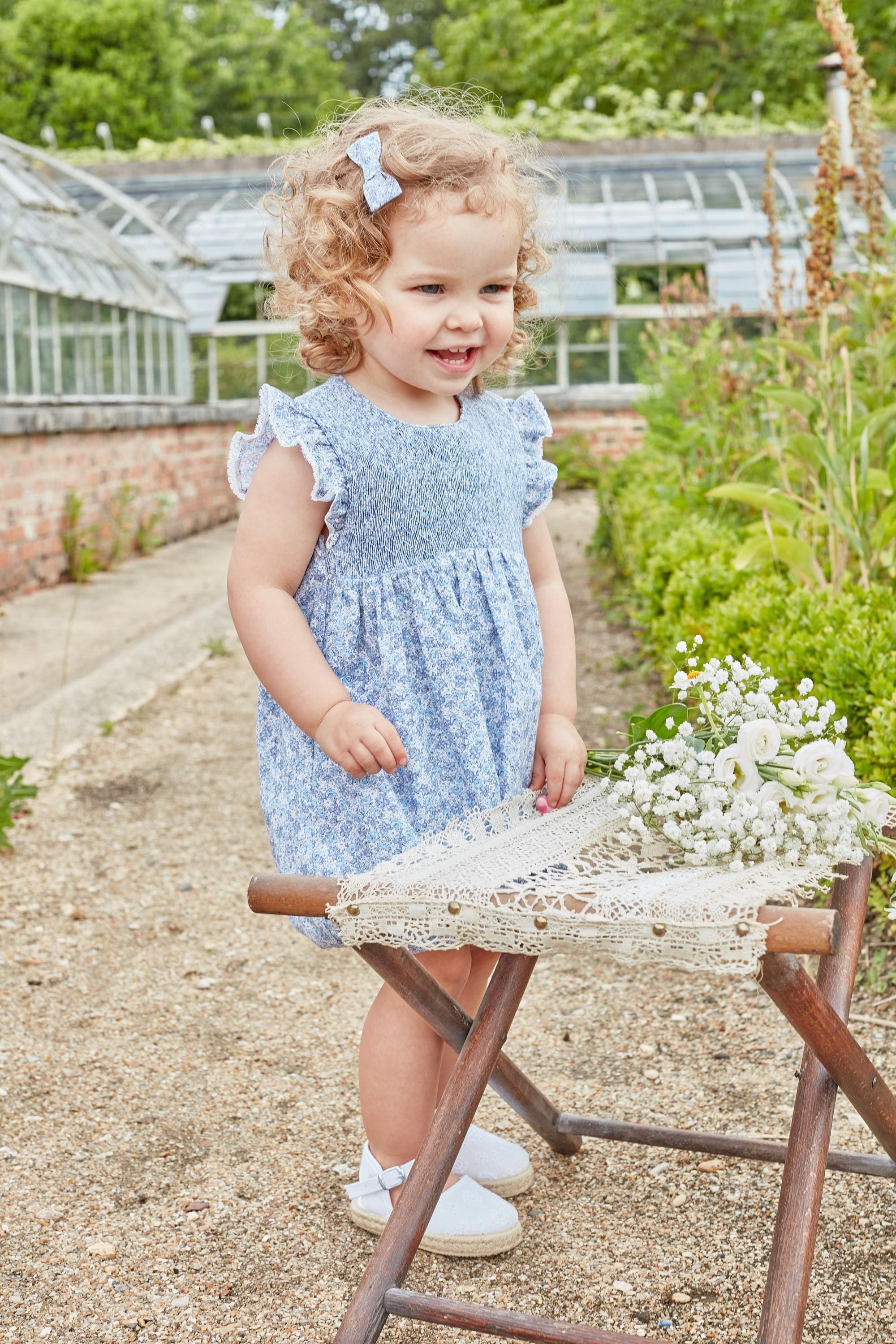 Capucine, Baby girl's romper, round neck, smocked bust, ruffled armhole with lace finish, 3 snaps on the bottom, in small blue flower print